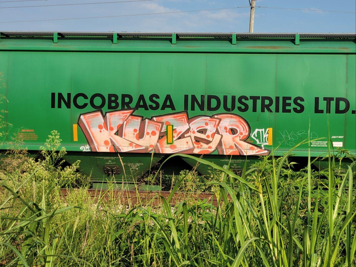 On a green rail car labeled Incobrasa Industries, KUZER in light orange funky block letters with brought orange edges and spots.