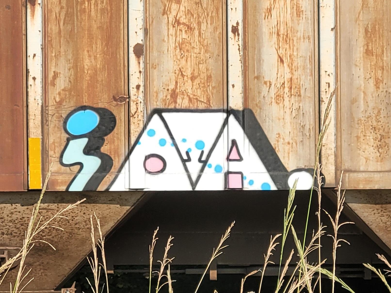 A light blue shape like a blunted lightning bolt has a brought blue circle on top like a head. To the right, three white isosceles triangles squished together so that the middle one is wedged upside down between the other two. The left triangle has a pink circle dead center in it. The right triangle has a pink triangle and square positioned to make it into an A. The middle triangle seems to contain two little twig arms coming from the other two triangles such that they seem to be doing a high five. An irregular stream of blue bubbles flows diagonally upper left to lower right across the triangles. 

Then to the right, a little circle like a period at the end of the A.